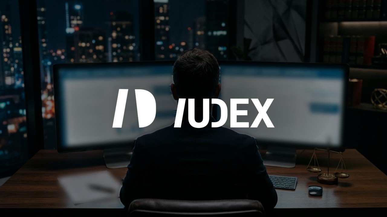 Un abogado frente a dos monitores en una oficina de noche, con el logotipo de IUDEX